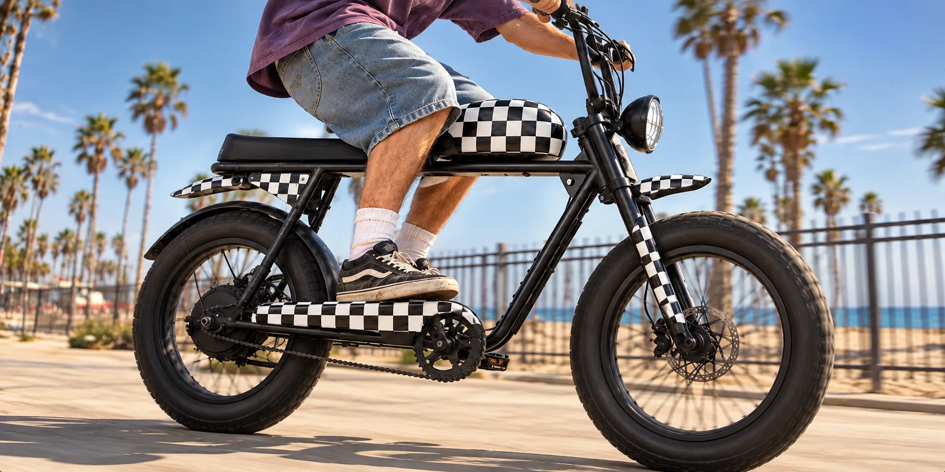 Rider on a checkered Super73 S2 riding a beach boardwalk past palm trees
